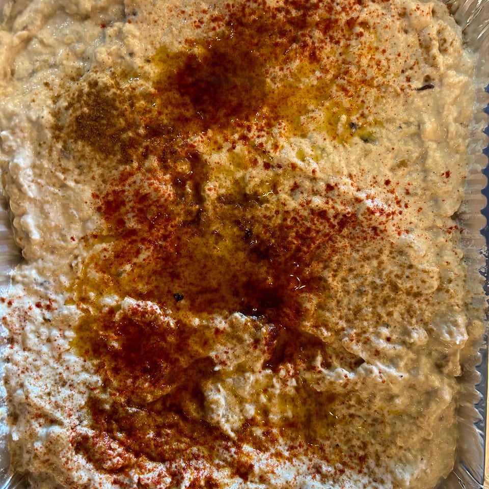 Creamy baba ghanoush in a foil container, drizzled with olive oil and sprinkled with red paprika.