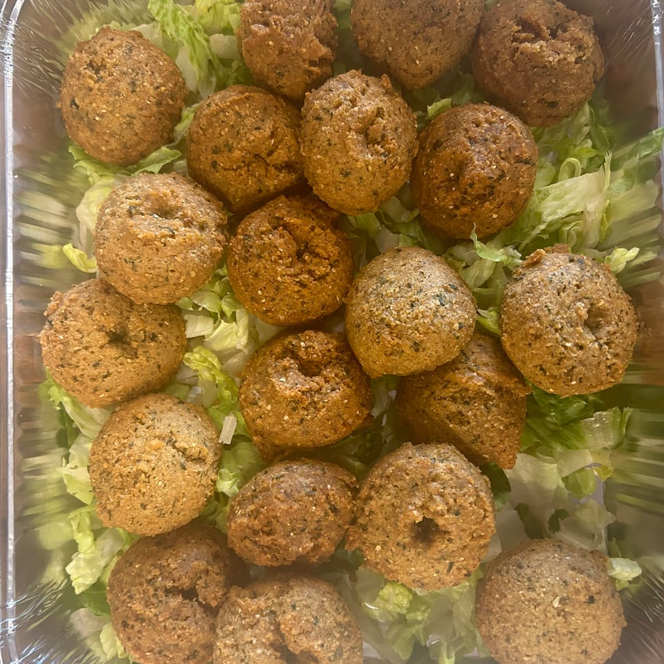 A catering tray filled with numerous golden-brown falafel balls resting on a bed of shredded lettuce.