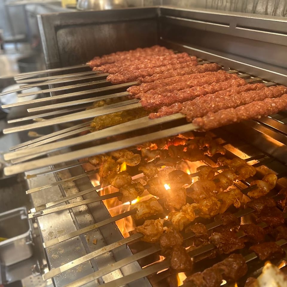 Skewers of various meats, including ground meat, chicken, and beef, grilling over flames.