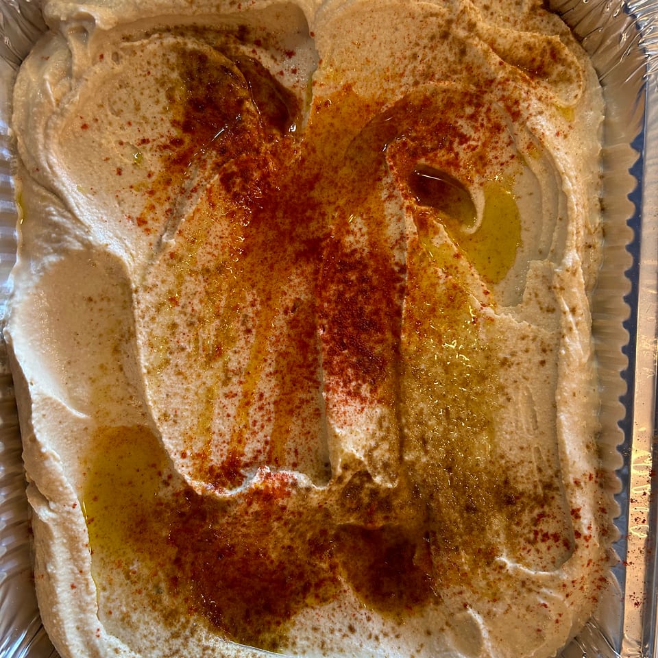 Creamy hummus in a foil container, drizzled with olive oil and sprinkled with paprika.