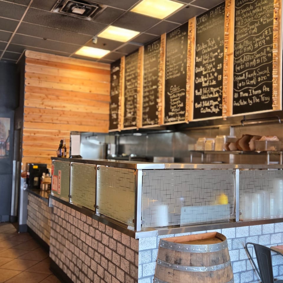 Restaurant interior with a brick counter, wooden barrel, and menu boards displaying food options.