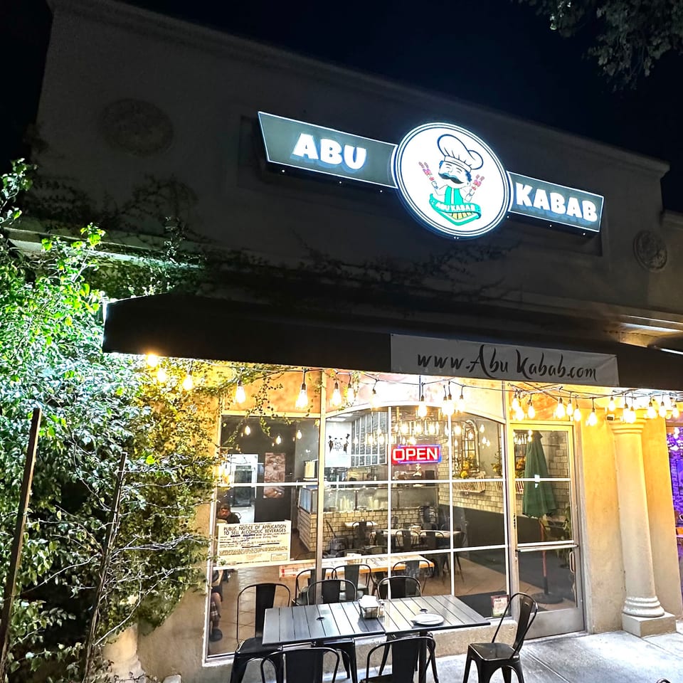 Exterior of Abu Kabab restaurant at night, with outdoor seating and an illuminated sign.