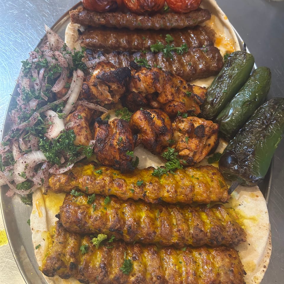 A platter of various grilled kebabs, including chicken, kofta, and beef, with roasted tomatoes and peppers.