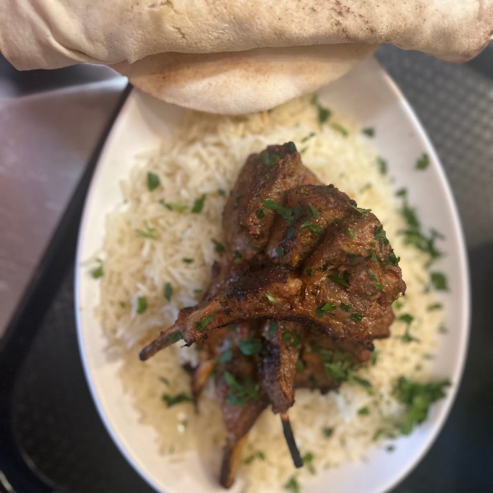 Grilled lamb chops with rice and parsley, served with pita bread on a white plate.